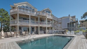 A multi-story building with a pool area, including a wooden deck, lounge chairs, and a statue. - 1559 - Sound Retreat - Spacious Corolla Soundfront w/ Sunset Views & Pool (Corolla)