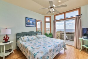 A bedroom with a bed, a ceiling fan, a TV, a balcony with a view, and a painting on the wall.