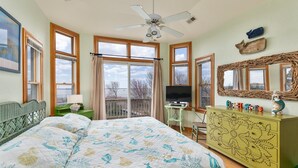 A bedroom with a bed, a dresser, a television, and large windows. - 1559 - Sound Retreat - Spacious Corolla Soundfront w/ Sunset Views & Pool (Corolla)