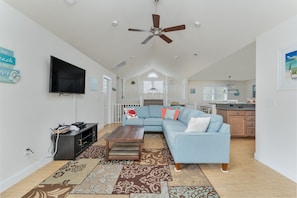A spacious living room with a sectional sofa, a flat-screen TV, a ceiling fan, and a patterned rug.
