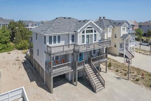 Uma casa na praia com varanda, escada e vista para a praia.