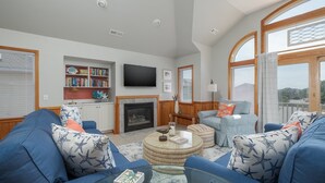 A living room with a fireplace, a television, and a bookshelf. - 1618 - Dune Buggy - Walk to Beach | Private Pool & Hot Tub (Corolla)