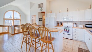 Una cocina con armarios blancos, una mesa de comedor de madera con sillas y un ventanal grande.