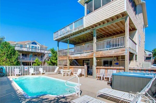 A two-story building with a pool area, outdoor seating, and a view of other buildings.