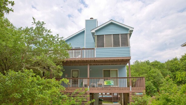A two-story house with a balcony, surrounded by lush greenery. - 1758 - Chesapeake Colony Escape - Dog-Friendly Corolla Retreat | Pool & Hot Tub (Corolla)
