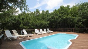 A swimming pool with a wooden deck, surrounded by trees and equipped with white lounge chairs. - 1758 - Chesapeake Colony Escape - Dog-Friendly Corolla Retreat | Pool & Hot Tub (Corolla)