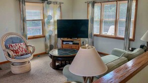 A living room with a television, a sofa, a chair, and a lamp. - 1758 - Chesapeake Colony Escape - Dog-Friendly Corolla Retreat | Pool & Hot Tub (Corolla)