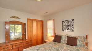 A bedroom with a bed, wooden dresser, wardrobe, and a window with blinds. - 1758 - Chesapeake Colony Escape - Dog-Friendly Corolla Retreat | Pool & Hot Tub (Corolla)
