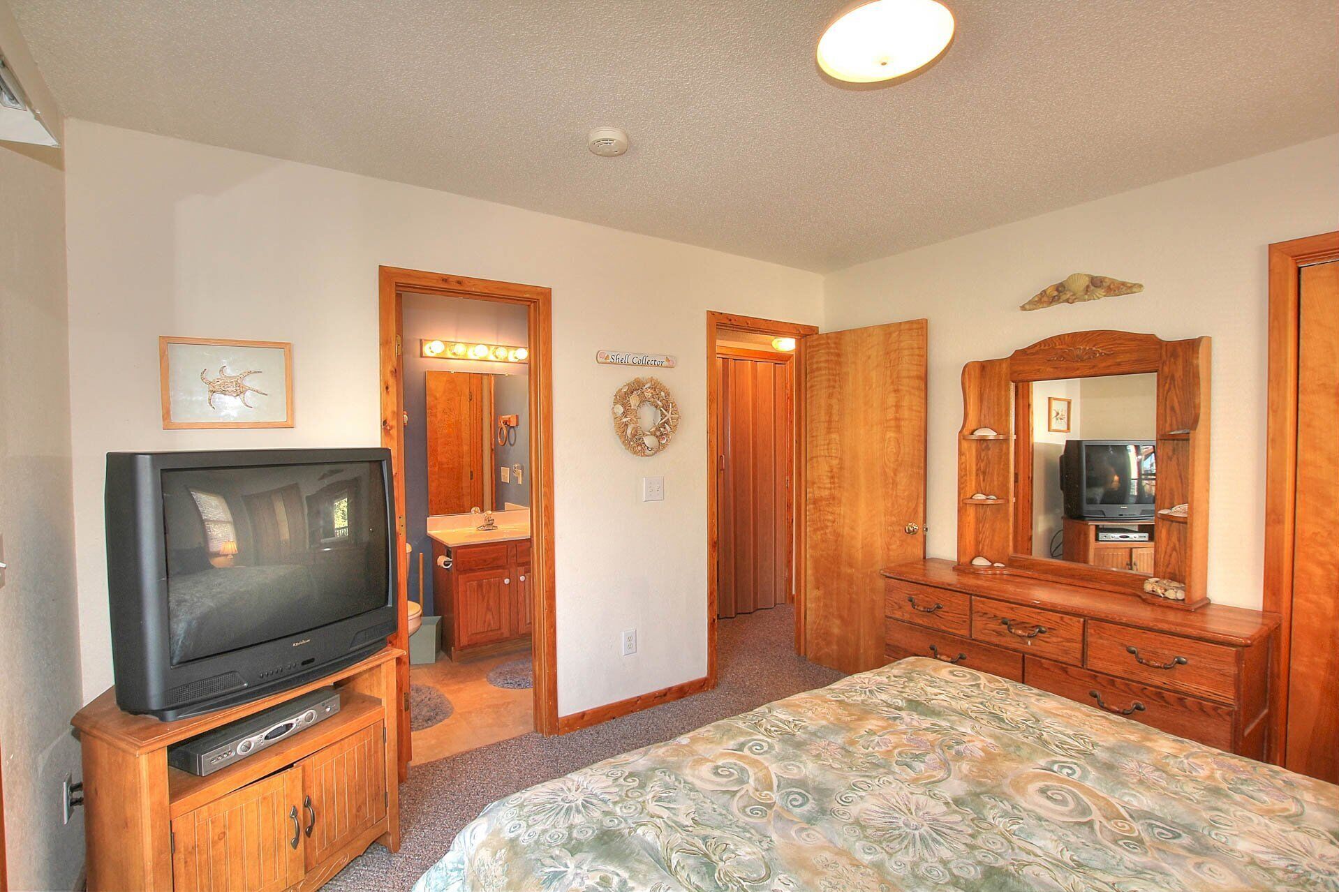 A bedroom with a television, wooden dresser, and a large mirror.