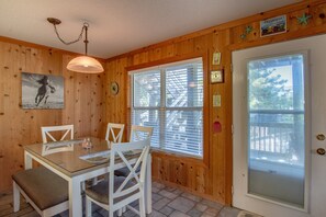 Ein Holzinterieur mit einem Esstisch, Stühlen, einer Deckenleuchte, einem Fenster mit Jalousien und einer Tür mit Fenster.