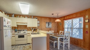 Eine Küche mit Holzwänden, einem Kühlschrank, einem Herd und einem Essbereich mit Stühlen und einem Tisch.