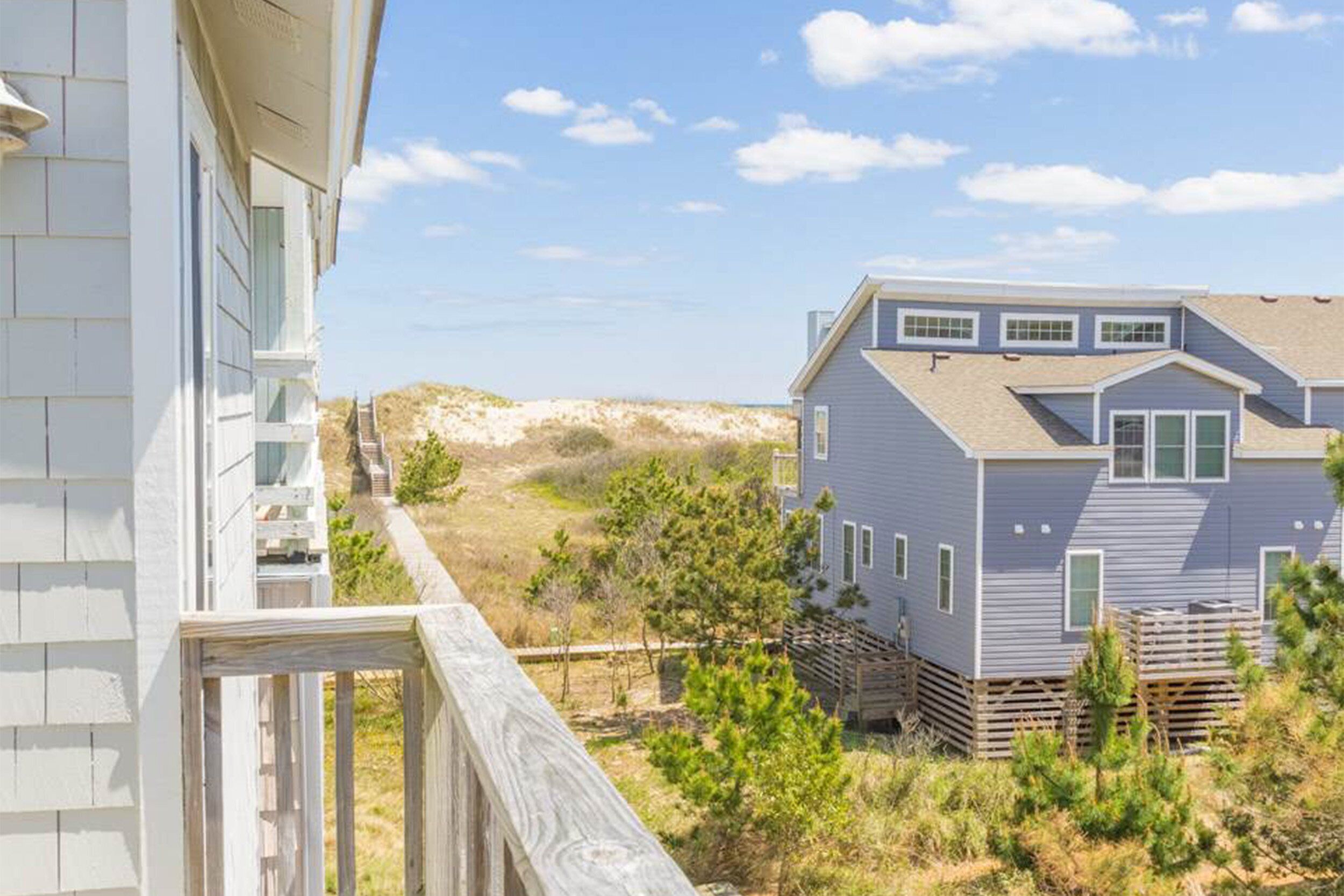 Ein zweistöckiges Haus mit Balkon, eingebettet in eine natürliche Landschaft und Dünen.