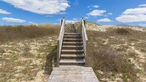 Una escalera de madera que lleva a una zona de playa, bajo un cielo despejado.