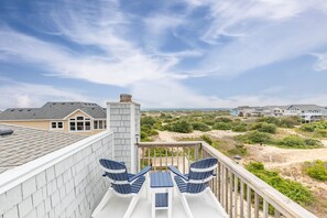 A balcony with two Adirondack chairs and a small table, overlooking a beach and other buildings. - 1849 - Dream Come True - Dog-Friendly Corolla Escape w/ Hot Tub (Corolla)