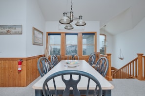 Un espace repas comprenant une longue table, des chaises, un lustre, un extincteur, une fenêtre et un escalier en bois.