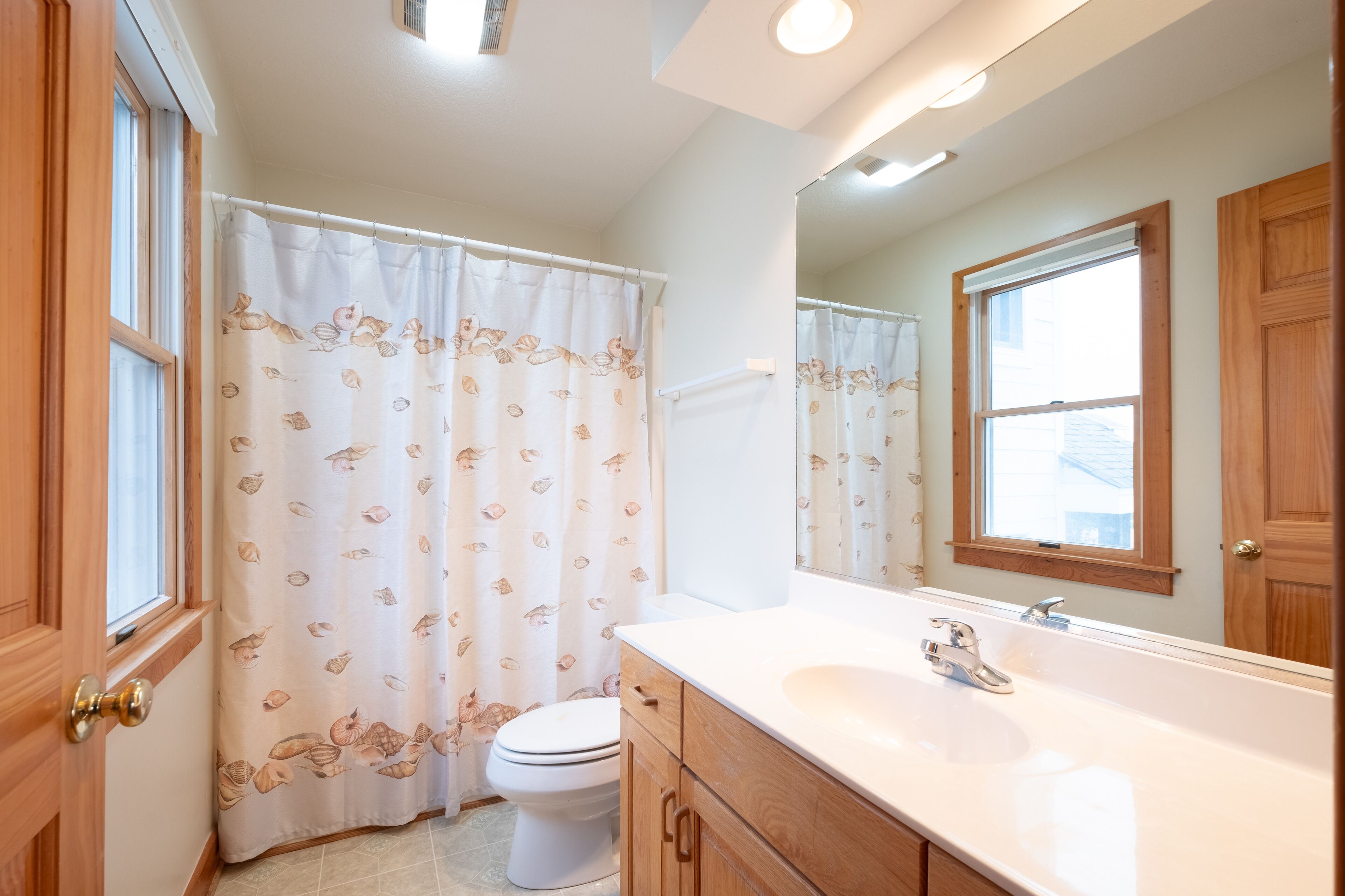 A bathroom with a toilet, a sink, a mirror, and a shower curtain with a leaf pattern.