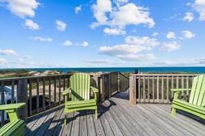 Une terrasse en bois avec des chaises vertes et une balustrade en bois donnant sur une plage.