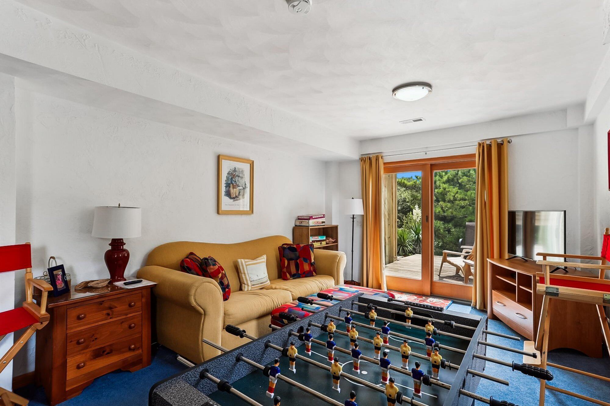 A room with a sofa, a foosball table, a TV, and a table with a lamp.