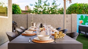 An outdoor dining area with a table set for four, surrounded by chairs, with a 'hello' sign on the table. - Designer 4BR w/ Free Heated Pool & Fire Pit,  Hiking Trail Right Off the Yard (Scottsdale)