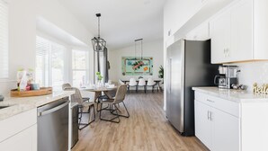 A modern kitchen with white cabinetry, a black refrigerator, and a dining area with a wooden table and chairs. - Designer 4BR w/ Free Heated Pool & Fire Pit,  Hiking Trail Right Off the Yard (Scottsdale)