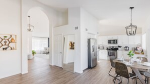 A modern kitchen with white cabinets, stainless steel appliances, and a dining area with a round table and wicker chairs. - Designer 4BR w/ Free Heated Pool & Fire Pit,  Hiking Trail Right Off the Yard (Scottsdale)