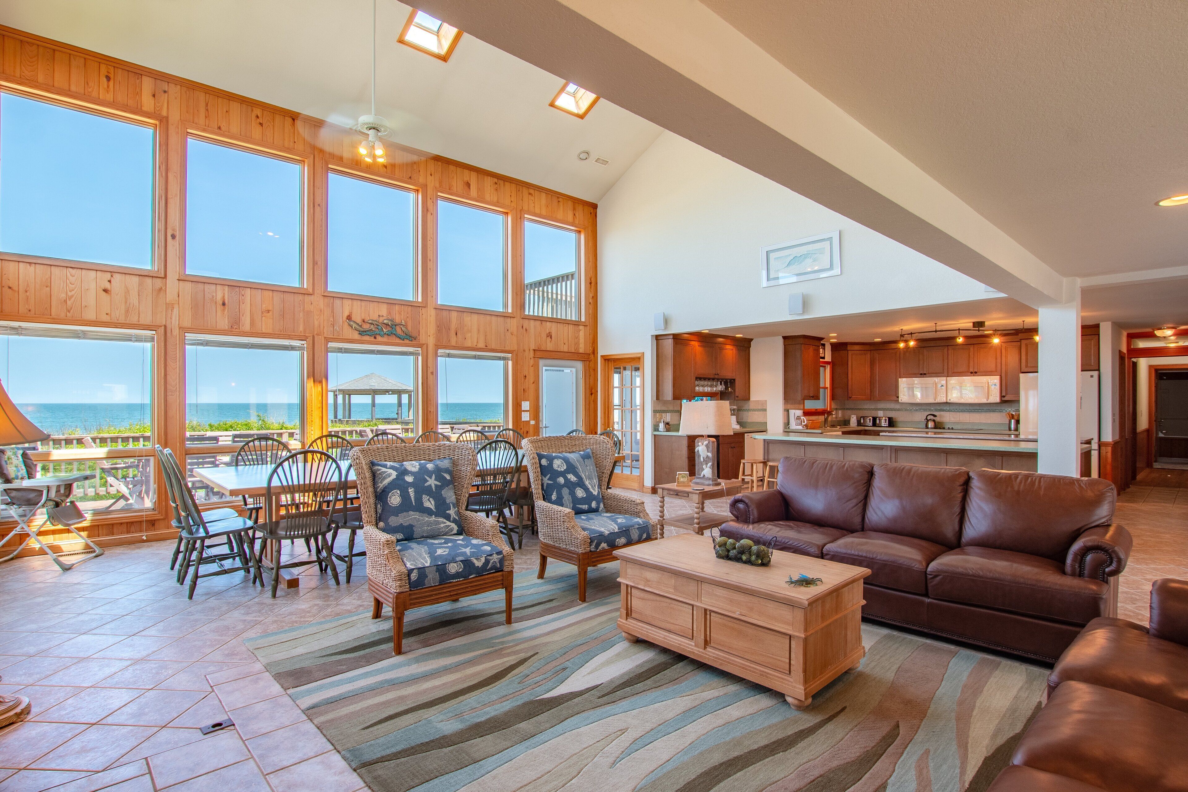 A spacious living room with large windows, a cozy seating area, and a kitchen in the background.