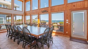 Un'ampia sala da pranzo con un grande tavolo di legno e sedie, ampie finestre e vista sull'oceano.