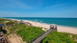 Una spiaggia con una passerella in legno, ombrelloni e un gazebo.