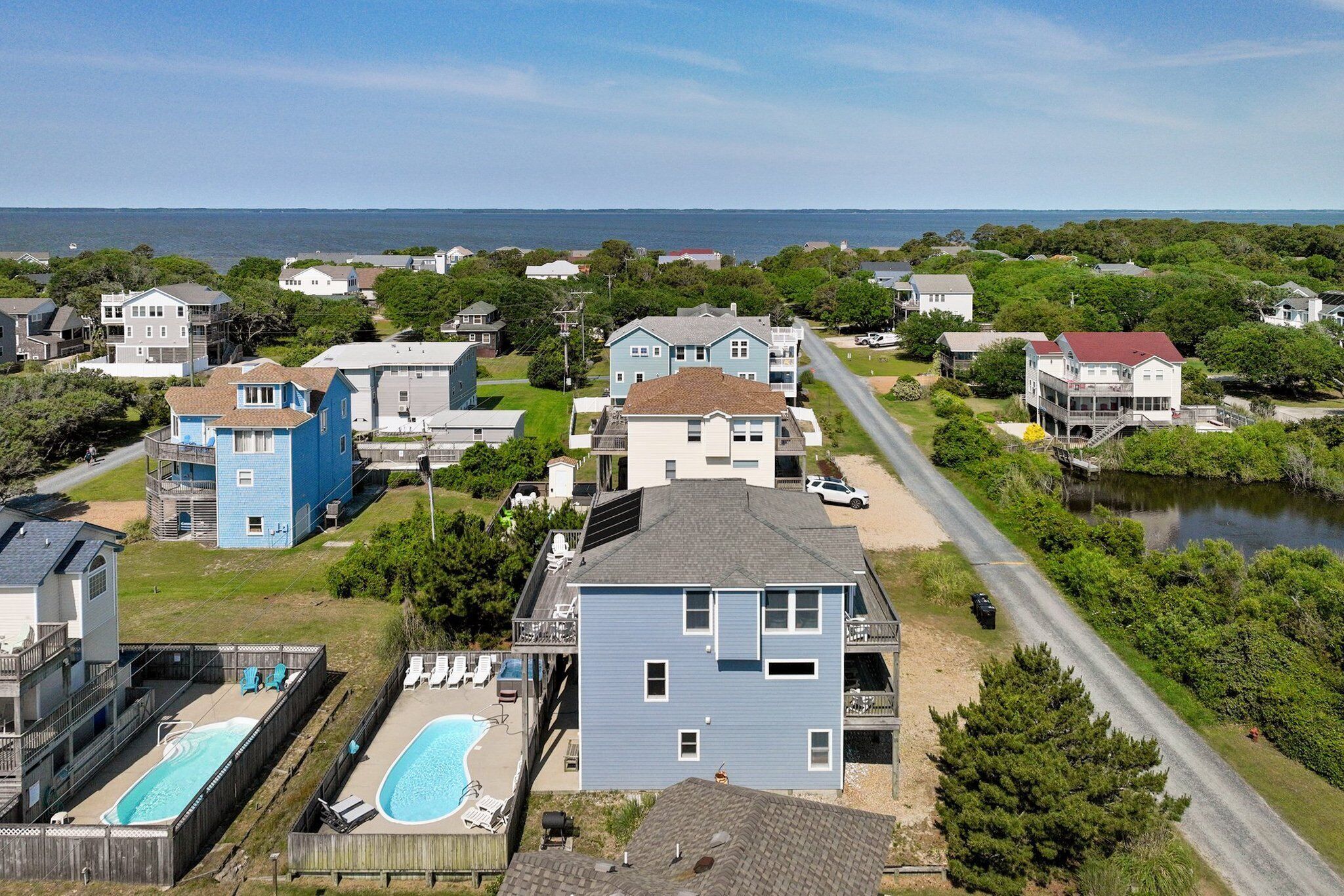 A residential area with houses, a swimming pool, and a road leading to a body of water.
