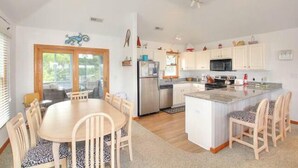 Una cocina moderna con armarios blancos, una isla central y un comedor con una mesa redonda y sillas.