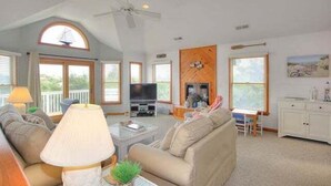 Amplia sala de estar con techo alto, ventanas grandes, chimenea y televisor.