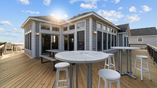 A modern house with a deck, large windows, and a round table with stools. - 2820 - Dabbling Duck - Spacious Duck Getaway | Pool, Hot Tub & More (Duck)
