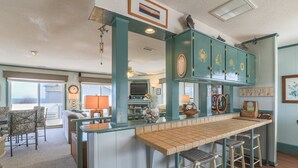 A kitchen with teal cabinets, a bar area with stools, and a view to the outside. - 2885 - Cobb Station, Oceanside home perched high on a rise with great ocean views & sea breezes (Duck)