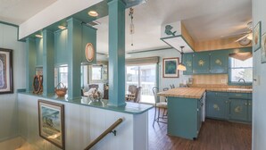 A kitchen with teal cabinetry, a wooden island, and a dining area with chairs. - 2885 - Cobb Station, Oceanside home perched high on a rise with great ocean views & sea breezes (Duck)