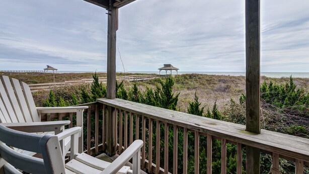 A wooden deck with two Adirondack chairs, overlooking a beach with dunes and two gazebos in the distance. - 2948 - Duck Nest, Perfect for smaller families or couples with unparalleled ocean views & amenities (Duck)