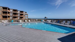 Une piscine dotée d’une terrasse en bois, de chaises longues et offrant une vue sur l’océan.