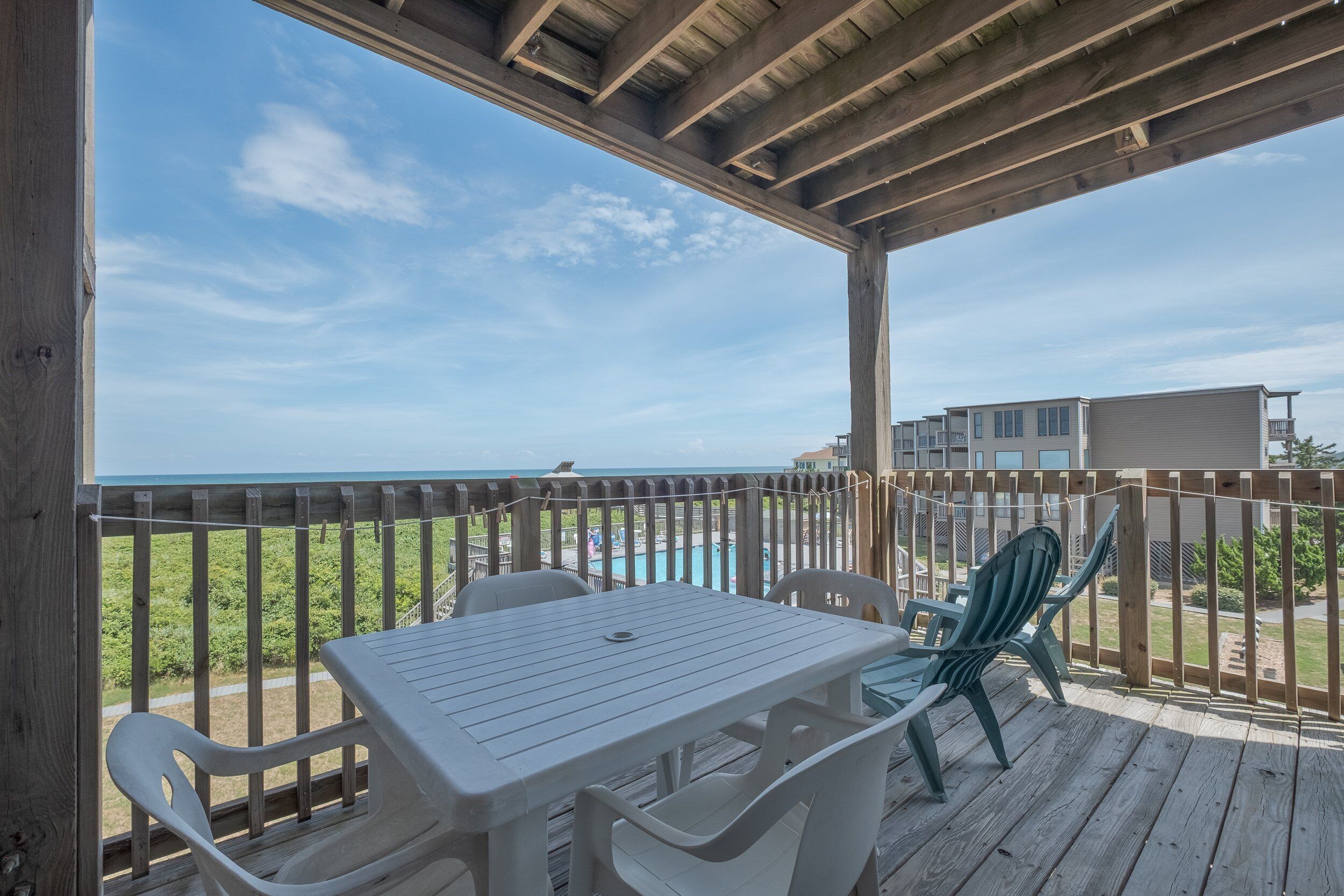 A covered outdoor area with a table and chairs, overlooking a beach and a pool.