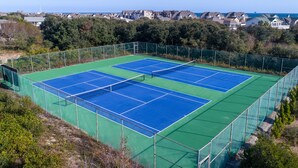 Un court de tennis avec un filet, entouré d’une clôture, et des maisons en arrière-plan.