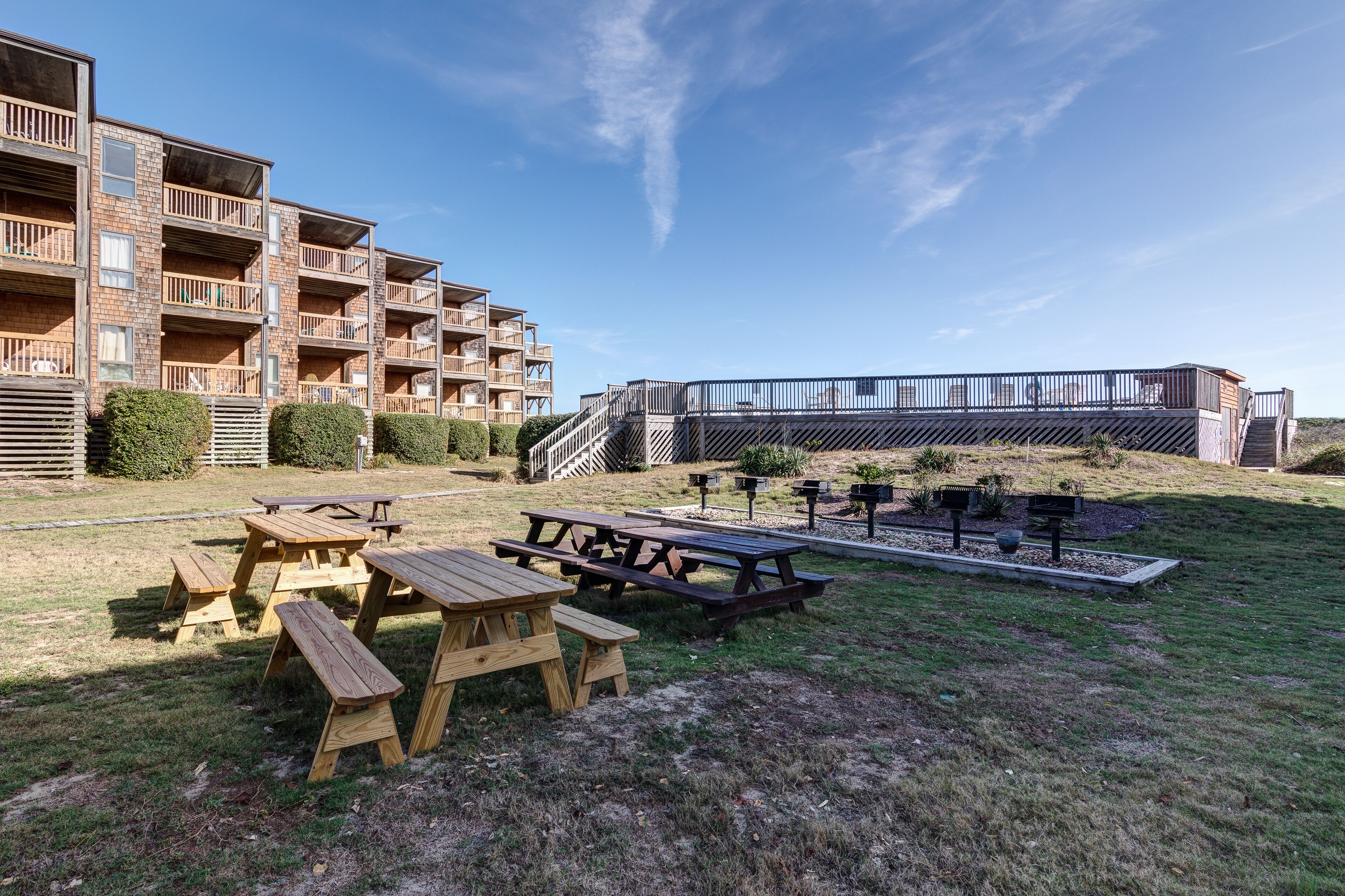 A residential building with multiple balconies, a wooden deck, and picnic tables in a grassy area.