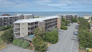 Un immeuble résidentiel à plusieurs étages, doté de balcons, d’un parking et offrant une vue sur l’océan.