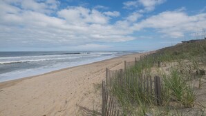 Une plage de sable avec une clôture en bois et de l’herbe au premier plan.