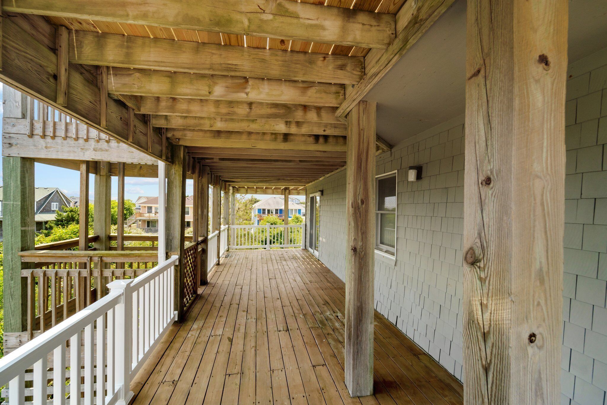 A covered wooden deck with a white railing, leading to a white-walled room with a window.