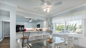 A modern kitchen with white cabinets, a black refrigerator, and a dining area with a glass table and white chairs. - 4104 - Sever's Hideaway, Cozy Coastal Retreat | Walkable Duck Location (Duck)