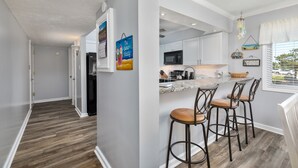A modern kitchen with white cabinets, a marble countertop, and a bar area with stools. - 4104 - Sever's Hideaway, Cozy Coastal Retreat | Walkable Duck Location (Duck)
