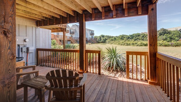 Una terraza de madera con vista a un paisaje cubierto de césped y un edificio al fondo.