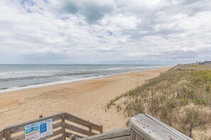 A beach with a wooden boardwalk leading to the water, a sandy shore, and a cloudy sky.