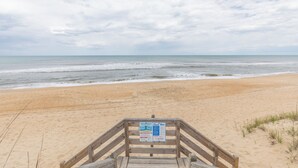 Pasarela de madera que lleva a una playa, con un letrero.