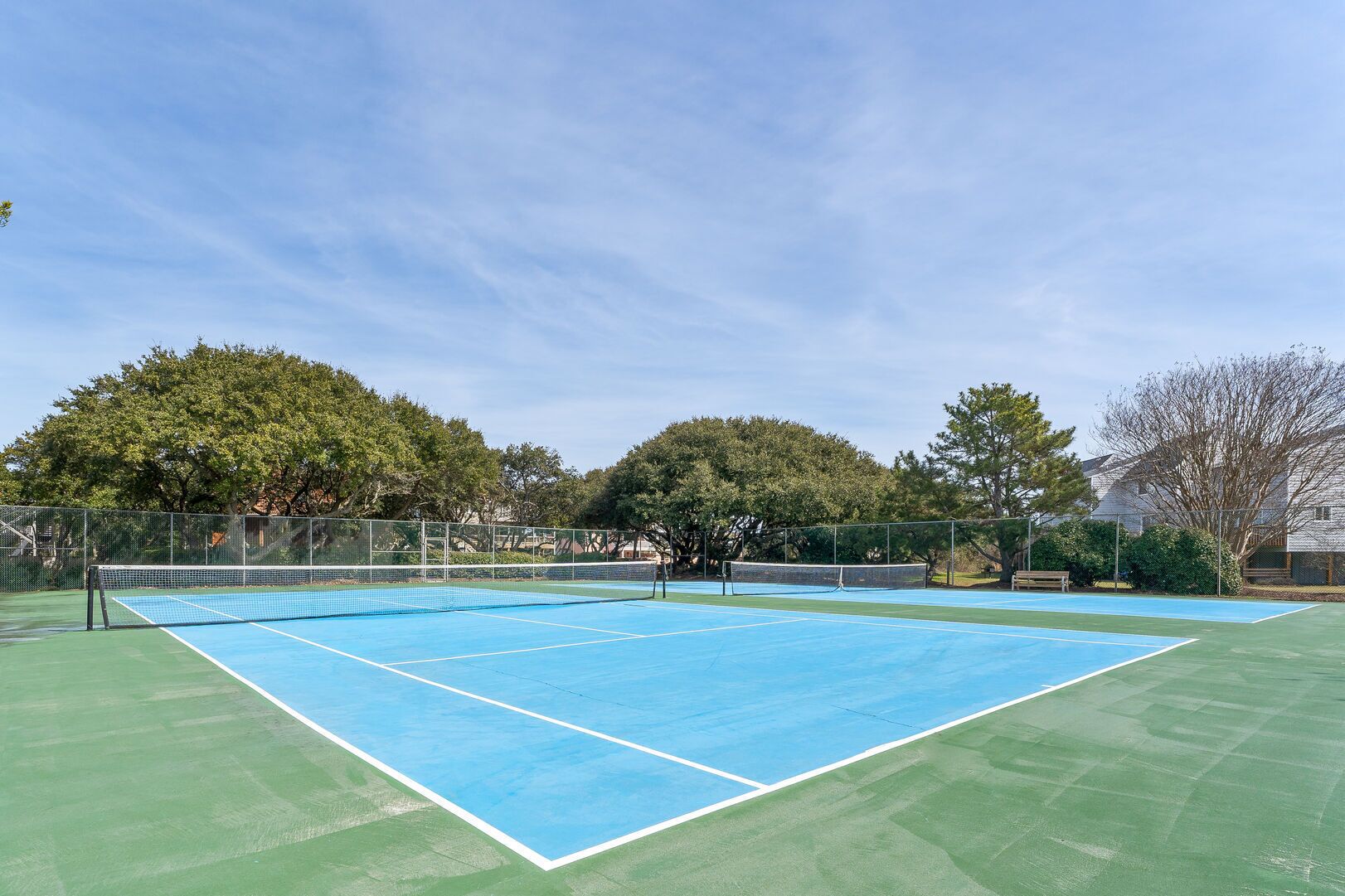 Un court de tennis avec un filet, entouré d’arbres et d’une clôture.
