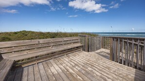 Ein hölzerner Steg führt zu einem Strand, der von einem klaren, blauen Himmel mit vereinzelten Wolken gesäumt wird.