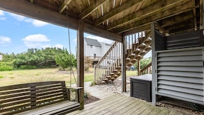 Eine Holzterrasse mit einer Schaukel, einer Treppe, die zu einem Haus führt, und einem überdachten Bereich mit einer Bank.